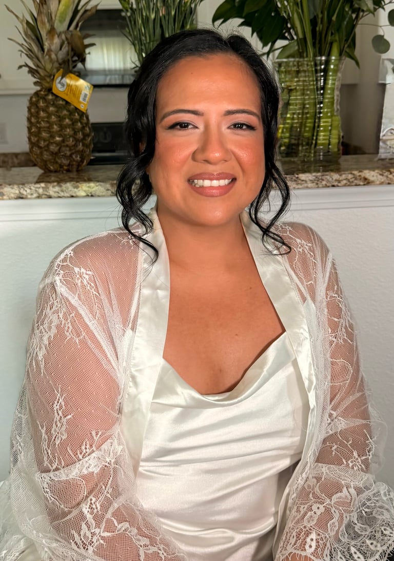Bridal transformation after - smiling woman with dark wavy hair wearing a white top and lace cardigan, indoors with potted plants in background