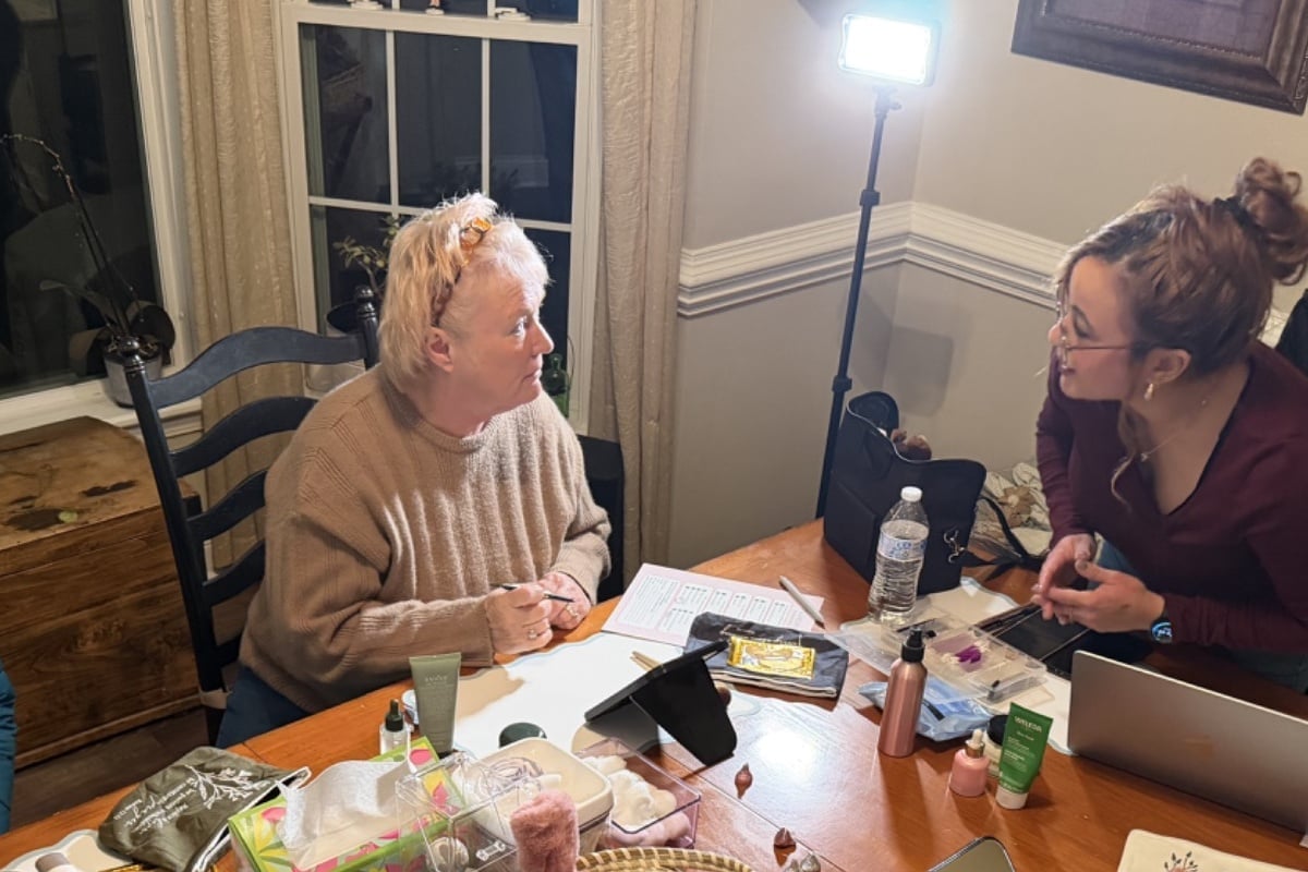 Two women sitting at a table with food and recording equipment, having a conversation in an indoor setting